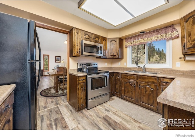 kitchen with stainless steel appliances, a sink, light wood finished floors, and light countertops