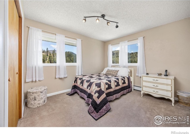 carpeted bedroom featuring a textured ceiling, baseboard heating, and baseboards