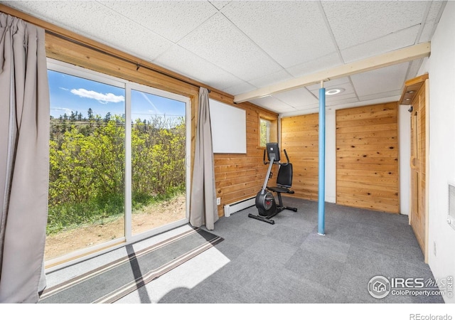 exercise area with wooden walls, carpet, a baseboard heating unit, and a drop ceiling