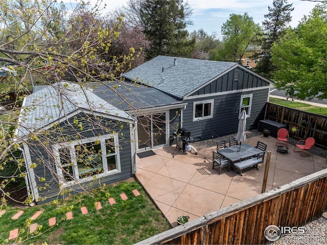 back of property with roof with shingles, board and batten siding, a patio area, and fence