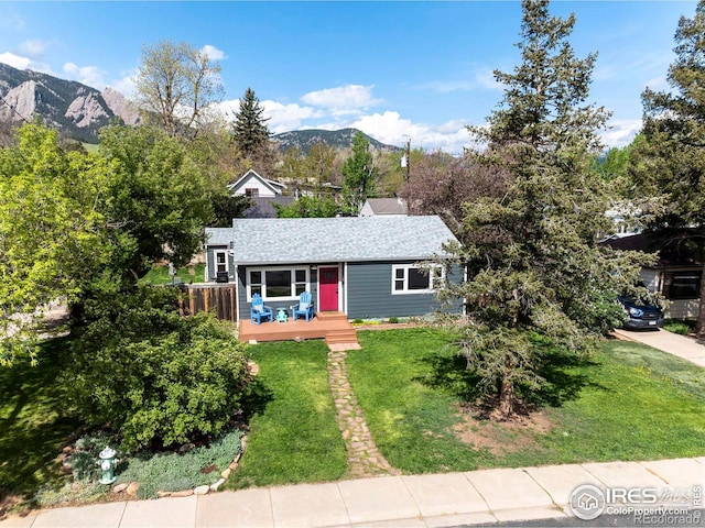 view of front facade featuring a deck with mountain view, a front yard, and roof with shingles