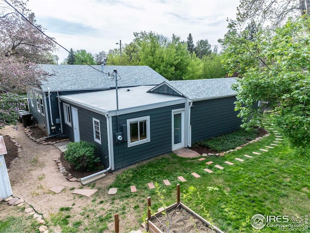 back of property with roof with shingles, a lawn, and a vegetable garden