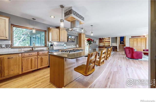 kitchen with a sink, light wood finished floors, stainless steel gas stovetop, tasteful backsplash, and a breakfast bar area