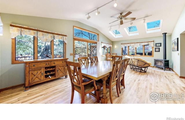dining room with track lighting, a wood stove, ceiling fan, a skylight, and lofted ceiling