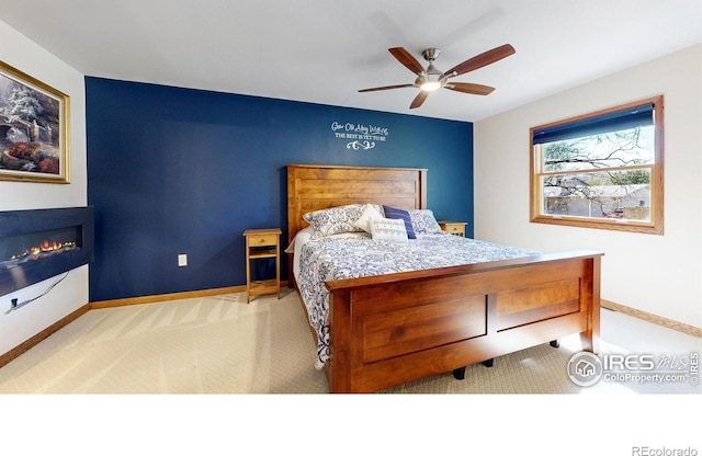 bedroom featuring carpet floors, baseboards, a glass covered fireplace, and a ceiling fan