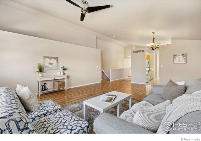 living room featuring vaulted ceiling, a chandelier, wood finished floors, ceiling fan, and baseboards
