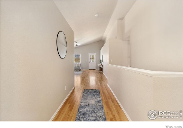 corridor with wood finished floors, lofted ceiling, and baseboards