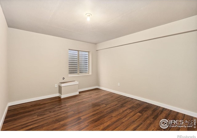 spare room featuring dark wood finished floors and baseboards