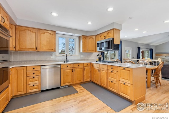 kitchen with appliances with stainless steel finishes, light wood-type flooring, a peninsula, decorative backsplash, and recessed lighting