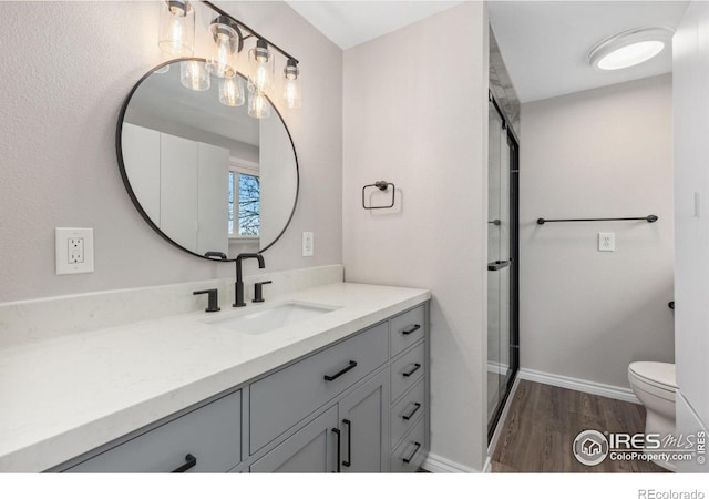 full bath featuring toilet, wood finished floors, vanity, baseboards, and a shower with shower door