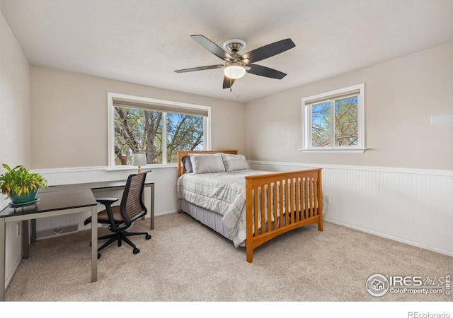 carpeted bedroom with wainscoting, ceiling fan, and an office area
