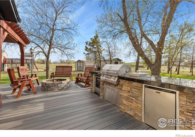 deck with area for grilling, a shed, an outdoor fire pit, and an outbuilding