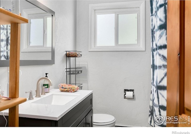 bathroom featuring plenty of natural light, toilet, vanity, and a textured wall