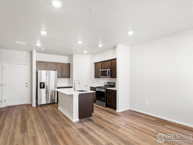 kitchen featuring appliances with stainless steel finishes, wood finished floors, dark brown cabinetry, a sink, and recessed lighting