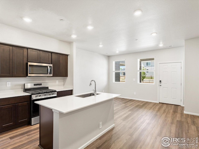 kitchen featuring stainless steel appliances, a sink, light wood-style flooring, dark brown cabinetry, and recessed lighting