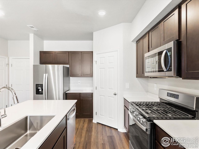 kitchen featuring appliances with stainless steel finishes, a sink, dark brown cabinets, dark wood-style flooring, and recessed lighting