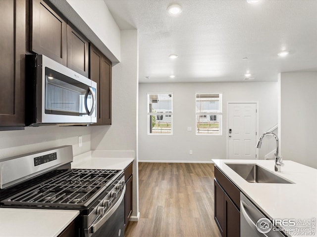 kitchen with stainless steel appliances, a sink, dark brown cabinets, light countertops, and light wood finished floors