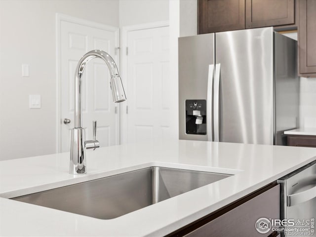 kitchen view of stainless steel appliances, a sink, light countertops, and dark brown cabinetry
