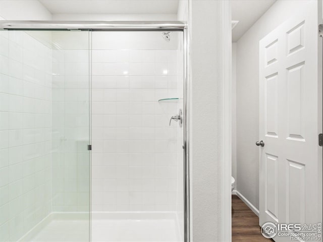 bathroom featuring a shower stall, wood finished floors, and toilet
