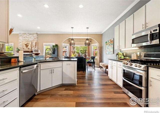 kitchen with stainless steel appliances, arched walkways, ornamental molding, a sink, and dark countertops