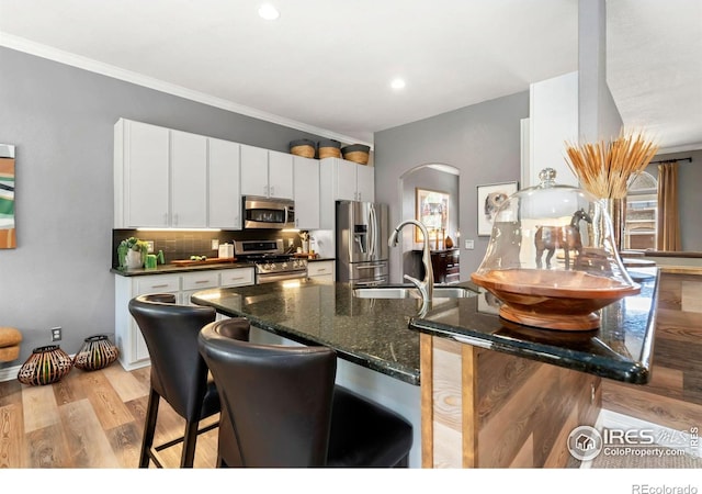 kitchen featuring appliances with stainless steel finishes, decorative backsplash, white cabinetry, arched walkways, and a kitchen breakfast bar