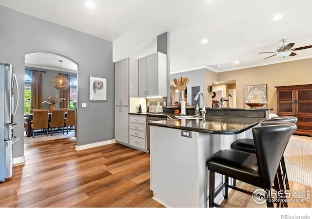 kitchen with a sink, arched walkways, stainless steel appliances, a peninsula, and light wood-type flooring