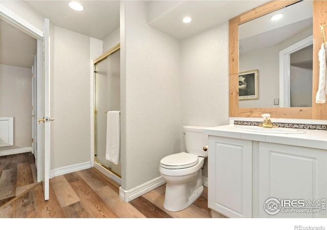 bathroom featuring toilet, wood finished floors, a stall shower, vanity, and recessed lighting