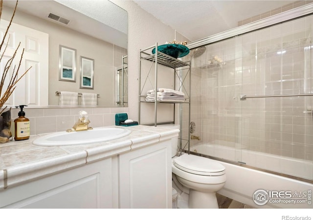 full bath featuring toilet, decorative backsplash, vanity, and combined bath / shower with glass door