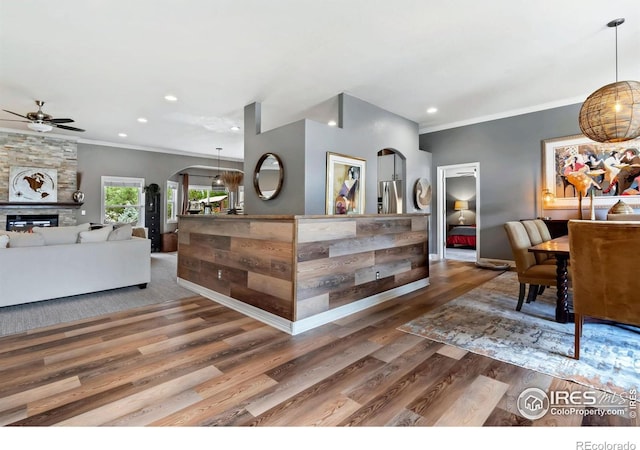 reception featuring arched walkways, ceiling fan, ornamental molding, recessed lighting, and a stone fireplace