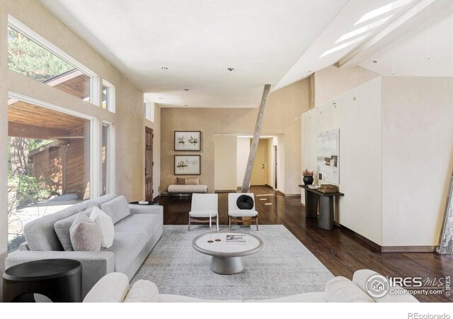 living area with dark wood-style floors, high vaulted ceiling, and baseboards