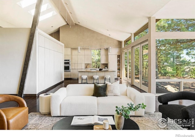 living area with high vaulted ceiling, a skylight, beam ceiling, and wood finished floors