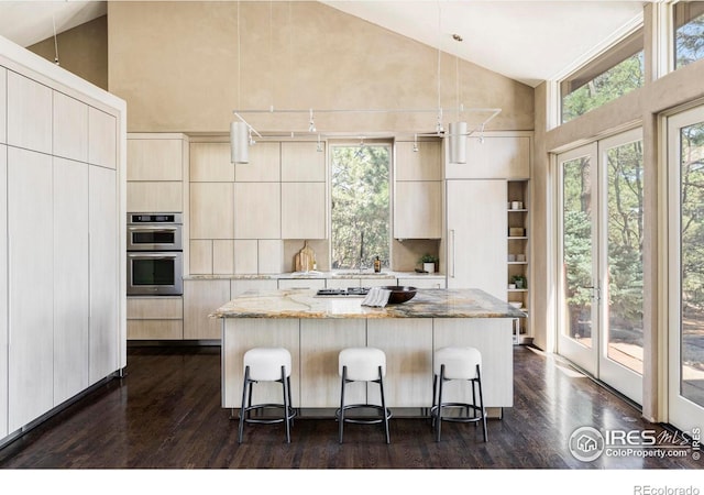 kitchen with high vaulted ceiling, modern cabinets, stainless steel double oven, healthy amount of natural light, and a kitchen island