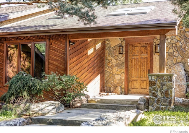 entrance to property with roof with shingles and stone siding