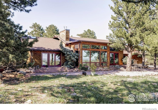 back of house featuring french doors, a chimney, and a lawn