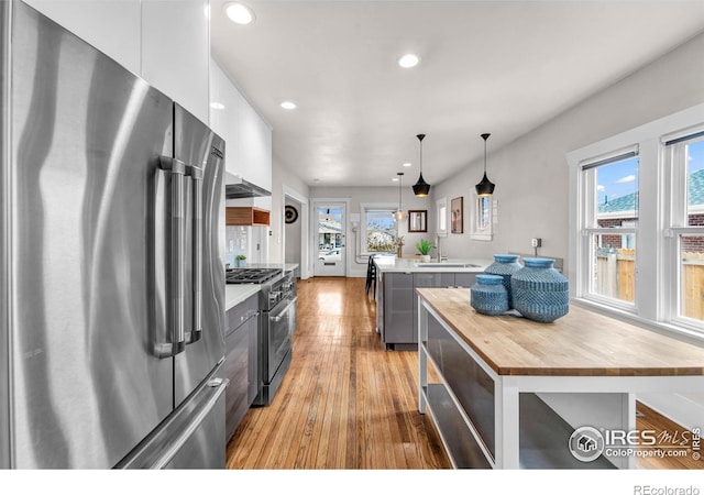 kitchen with high quality appliances, butcher block countertops, a kitchen island, light wood-style flooring, and recessed lighting