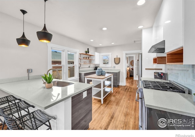 kitchen with a sink, under cabinet range hood, stainless steel range with gas cooktop, a breakfast bar, and a peninsula