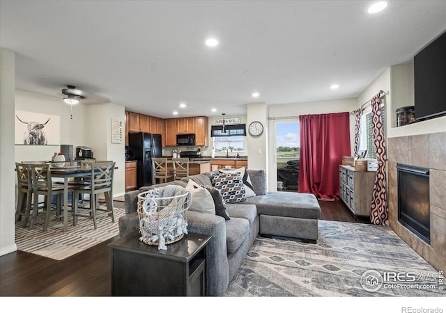 living room with a tile fireplace, dark wood-type flooring, recessed lighting, and a ceiling fan