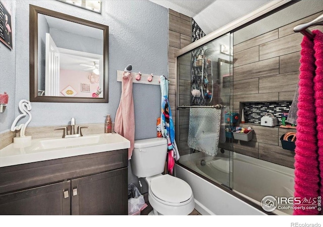 full bathroom featuring vanity, toilet, bath / shower combo with glass door, a textured wall, and a ceiling fan