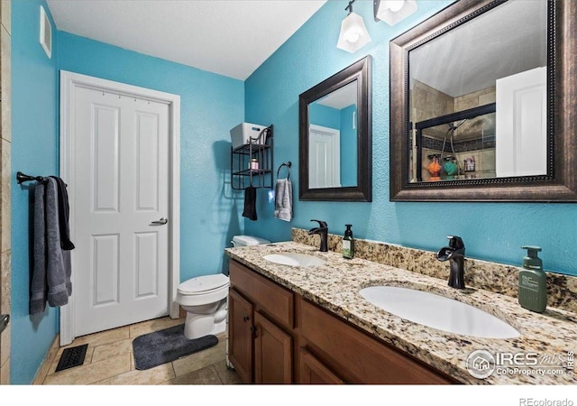 full bathroom with tiled shower, toilet, double vanity, and a textured wall