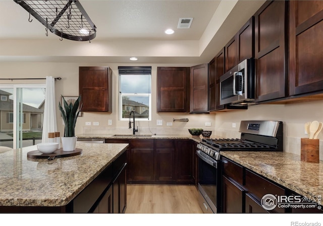 kitchen featuring a sink, stainless steel appliances, light wood-style floors, light stone counters, and dark brown cabinetry