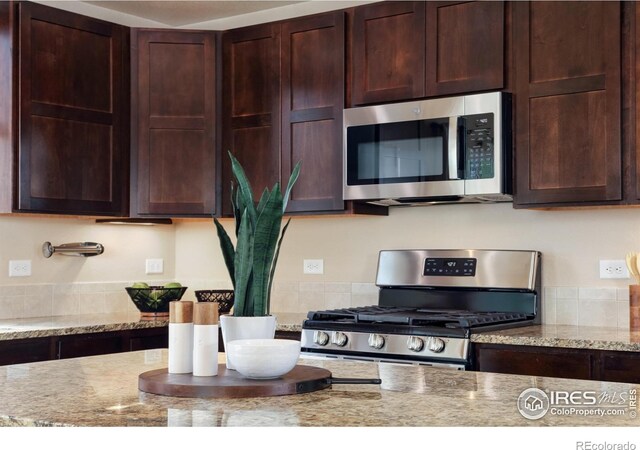 kitchen featuring stainless steel appliances, dark brown cabinetry, and light stone countertops