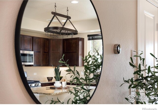 detailed view of stainless steel microwave, a textured wall, dark brown cabinetry, light stone countertops, and recessed lighting