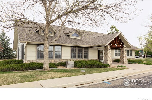 view of front of home featuring stone siding, roof with shingles, and a front lawn