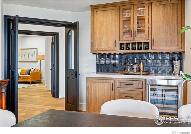 indoor wet bar featuring wine cooler, tasteful backsplash, light wood-style floors, and baseboards
