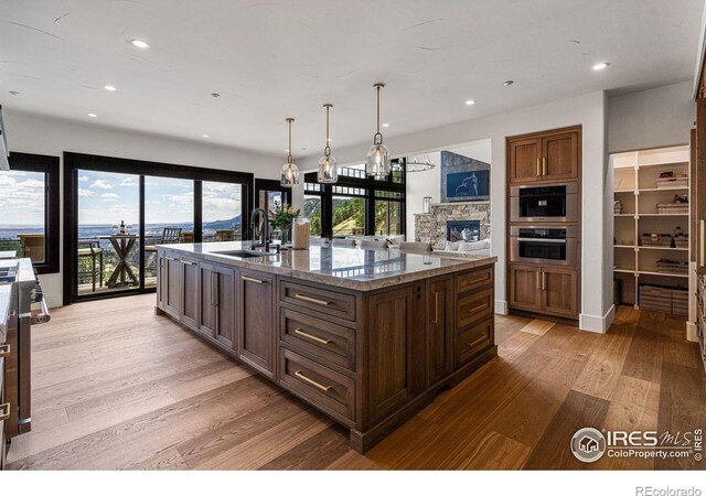 kitchen featuring light wood-style floors, a sink, recessed lighting, a center island with sink, and stone counters