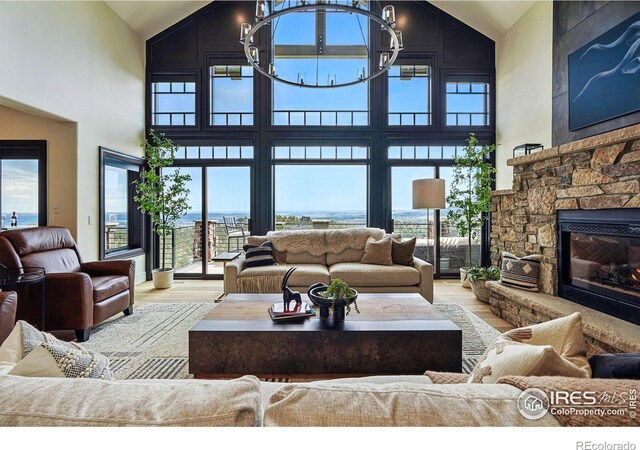 living room featuring high vaulted ceiling, wood finished floors, a stone fireplace, and a chandelier