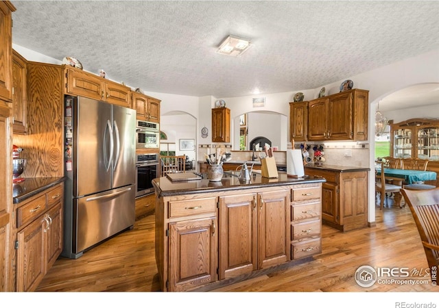 7309 Didrickson Ct, Fort Collins, CO 80528 - kitchen featuring stainless steel appliances, arched walkways, dark countertops, wood finished floors, and brown cabinets