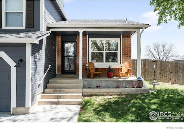 12506 Maria Cir, Broomfield, CO 80020 - doorway to property featuring a porch, fence, brick siding, and a shingled roof