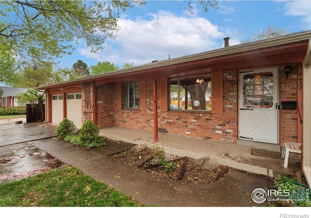 ranch-style home featuring brick siding, concrete driveway, an attached garage, and a porch