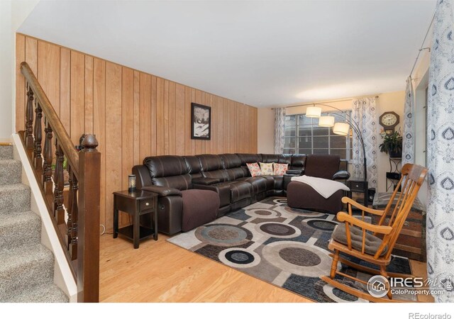 living room featuring wood finished floors, wooden walls, and stairs